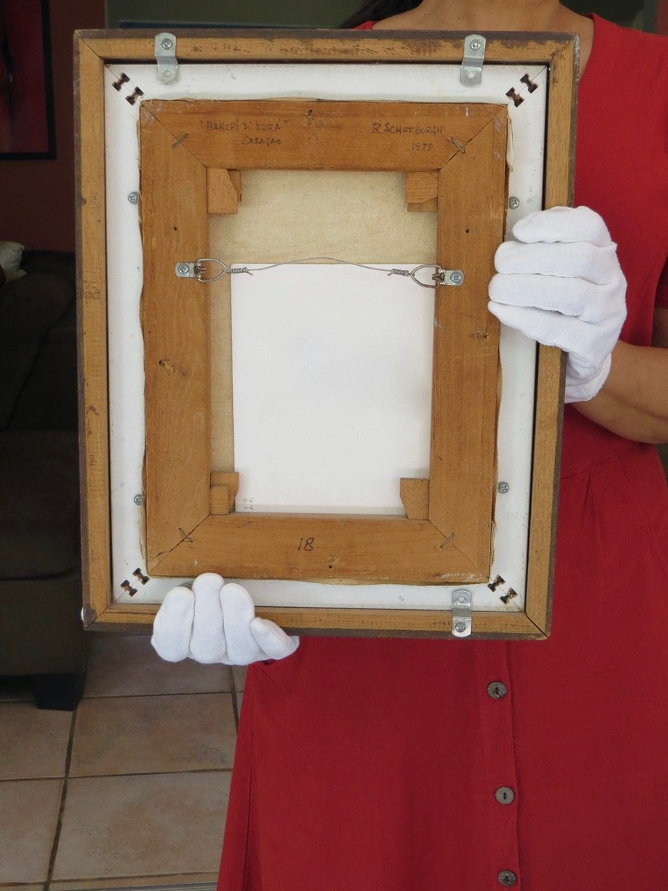 Toont achterkant schilderij, dat wordt vastgehouden met twee handen.